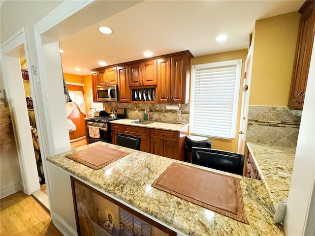 kitchen with light stone countertops, decorative backsplash, appliances with stainless steel finishes, light wood-style floors, and a sink