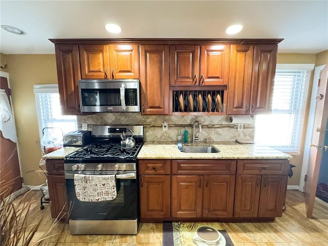 kitchen with light stone counters, plenty of natural light, appliances with stainless steel finishes, and a sink