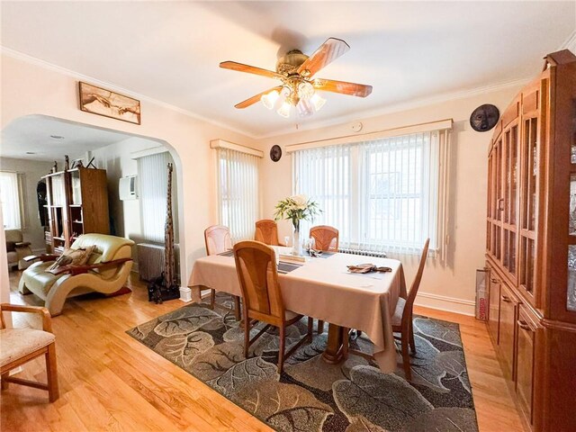 dining room featuring an AC wall unit, light wood-style flooring, arched walkways, crown molding, and baseboards