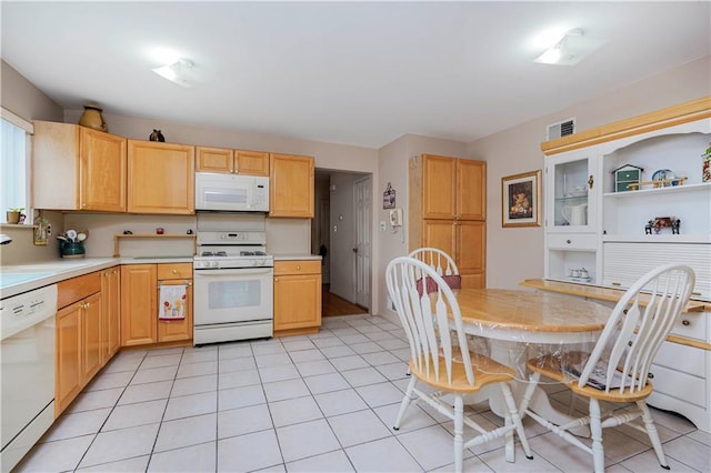 kitchen with light tile patterned floors, light brown cabinets, white appliances, and light countertops