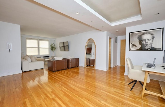 living area with a tray ceiling, light wood-type flooring, and baseboards