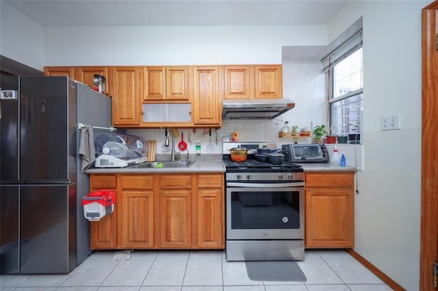 kitchen with light tile patterned flooring, a sink, decorative backsplash, under cabinet range hood, and appliances with stainless steel finishes