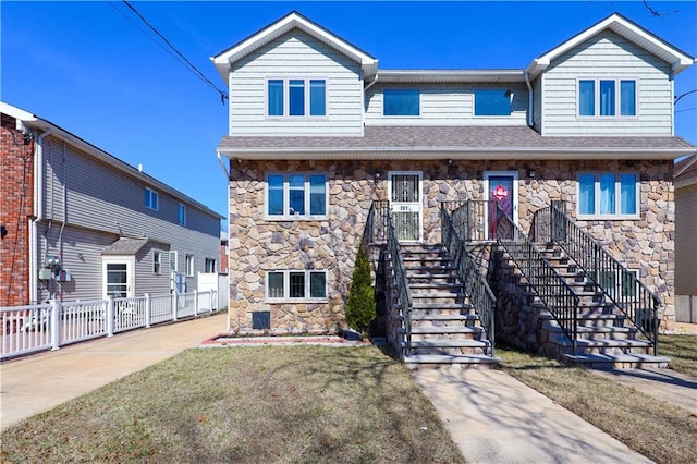 view of front of house featuring stairway, fence, stone siding, and a shingled roof