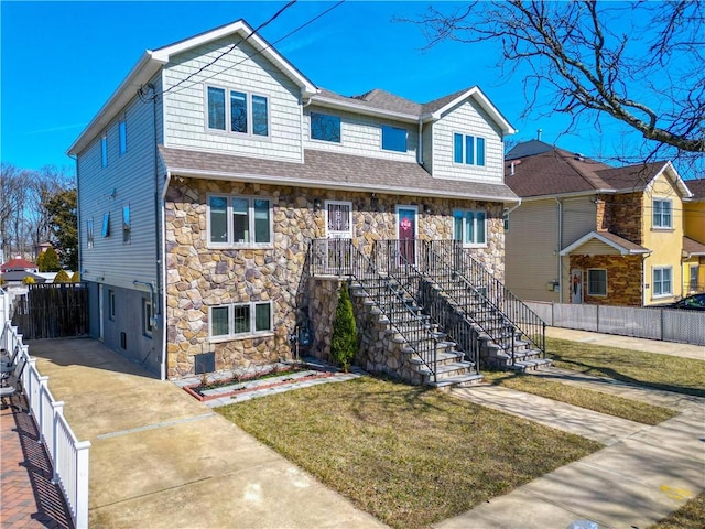 view of front of property with stone siding, a front yard, stairs, and fence