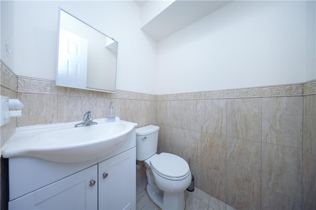 half bathroom featuring vanity, wainscoting, tile walls, toilet, and tile patterned floors