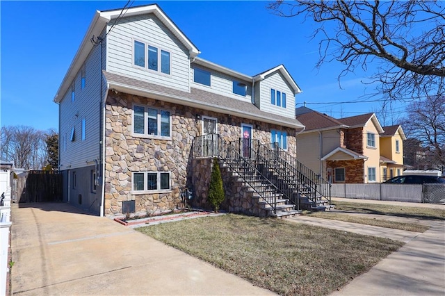 view of front of house with stairway, fence, concrete driveway, a front lawn, and stone siding