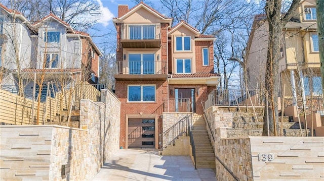 view of front facade with stairway, concrete driveway, an attached garage, brick siding, and a chimney