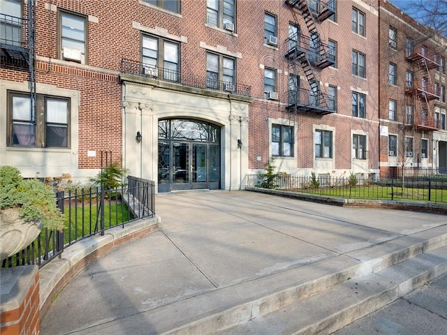 view of exterior entry with french doors, brick siding, and fence