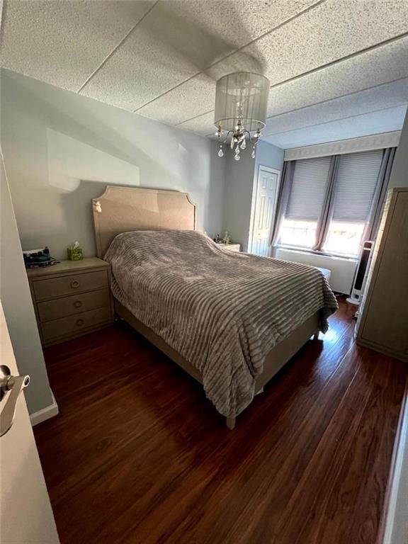 bedroom featuring dark wood-style floors, a drop ceiling, and an inviting chandelier