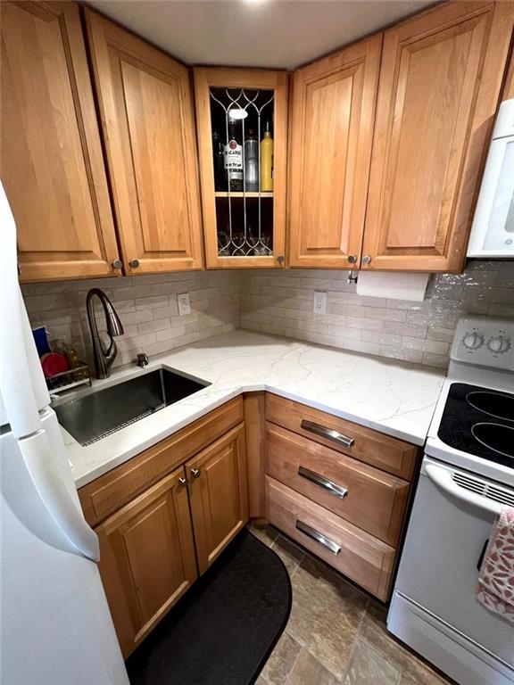 kitchen featuring backsplash, glass insert cabinets, light stone countertops, white appliances, and a sink