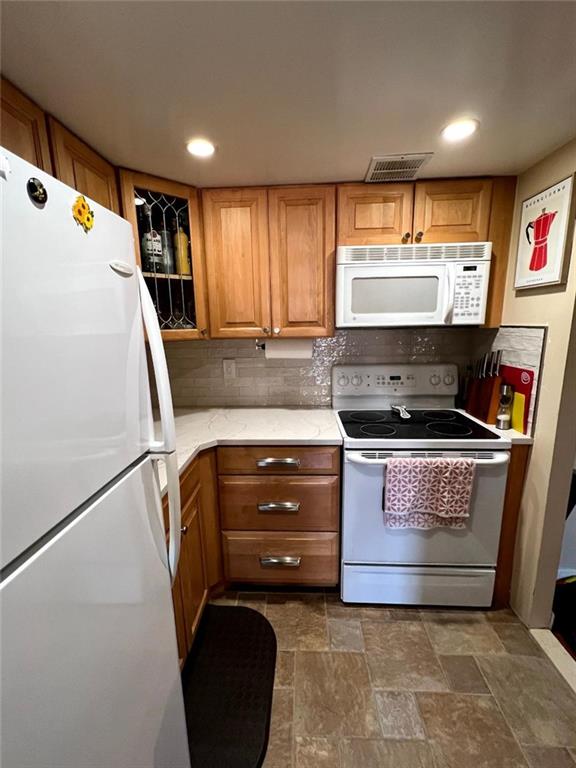 kitchen featuring white appliances, tasteful backsplash, brown cabinetry, and visible vents