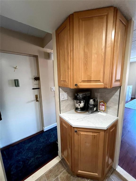 kitchen with decorative backsplash, light stone counters, baseboards, and brown cabinets