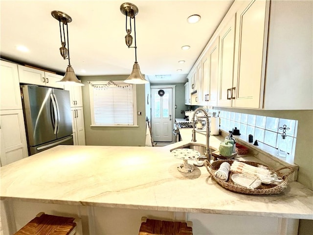 kitchen with light stone counters, hanging light fixtures, white cabinets, appliances with stainless steel finishes, and a kitchen breakfast bar