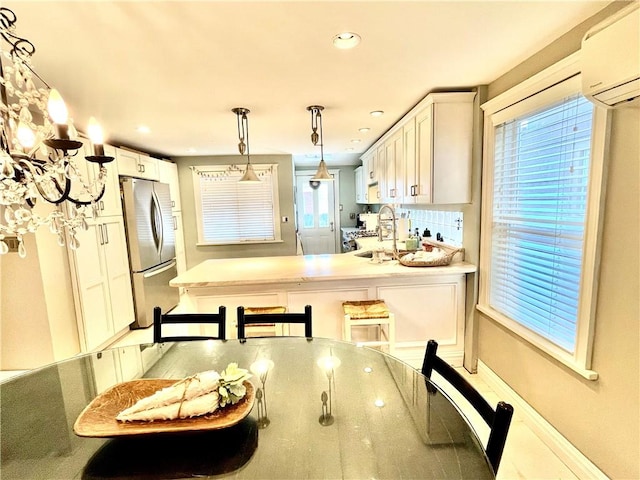 kitchen with a sink, a wall unit AC, freestanding refrigerator, a peninsula, and white cabinets