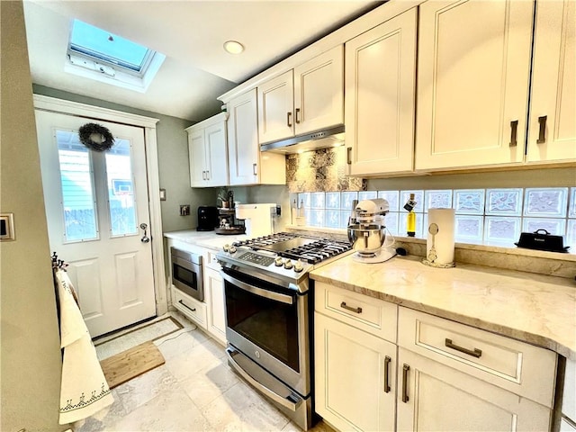 kitchen with under cabinet range hood, white cabinetry, stainless steel appliances, a skylight, and light stone countertops