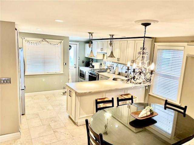 kitchen featuring a sink, light countertops, appliances with stainless steel finishes, pendant lighting, and a notable chandelier