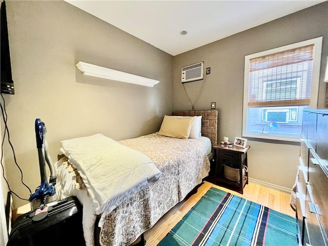 bedroom with a wall mounted air conditioner, baseboards, and wood finished floors