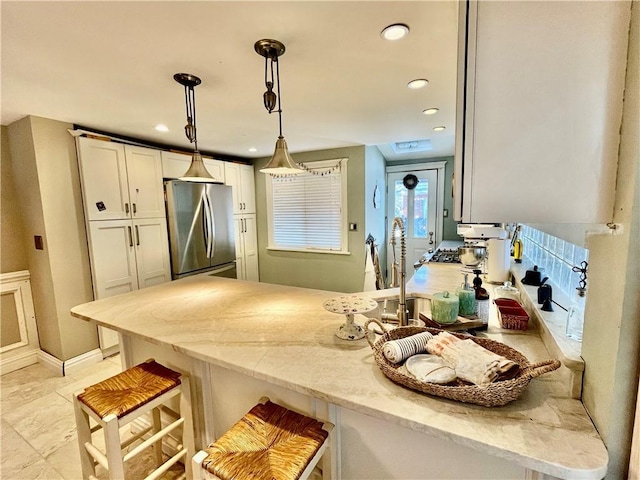 kitchen featuring light stone counters, a peninsula, freestanding refrigerator, white cabinetry, and decorative light fixtures