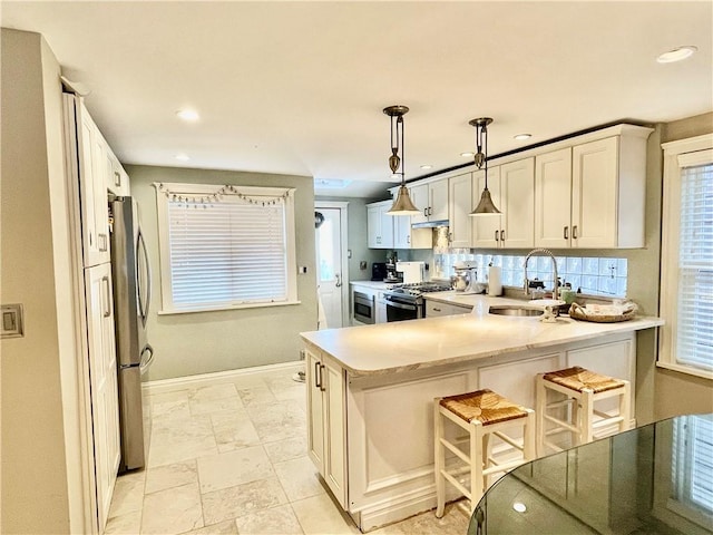 kitchen featuring baseboards, a peninsula, stainless steel appliances, light countertops, and a kitchen breakfast bar