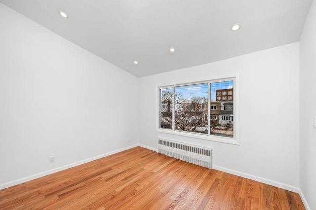 empty room featuring recessed lighting, radiator heating unit, light wood-style floors, and baseboards