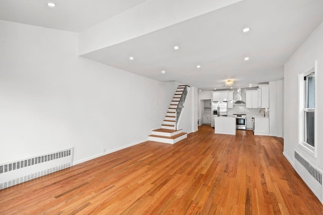 unfurnished living room with stairway, radiator heating unit, light wood-style floors, and recessed lighting