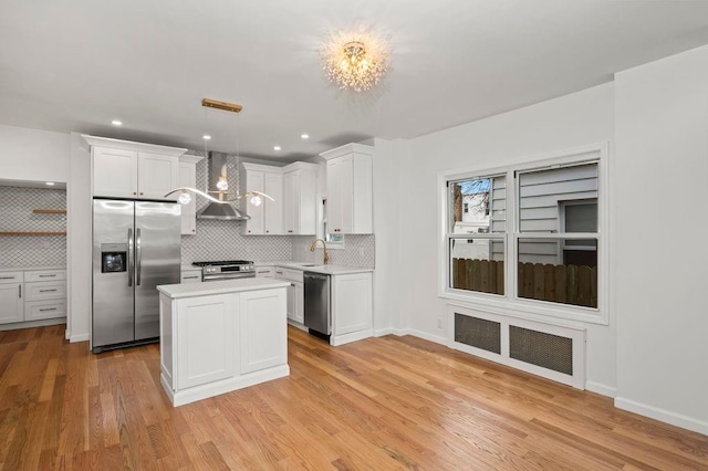 kitchen featuring white cabinetry, light wood-style floors, appliances with stainless steel finishes, wall chimney range hood, and light countertops