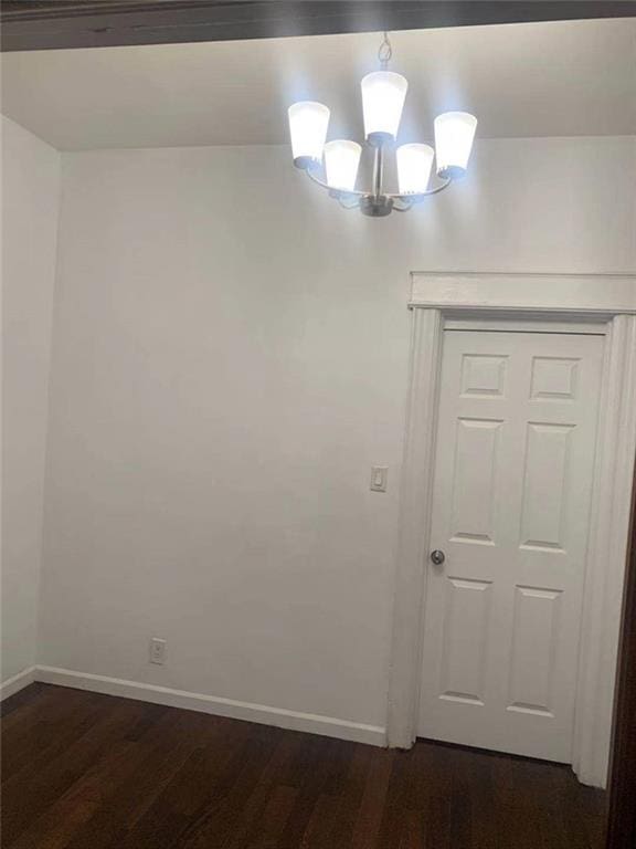 unfurnished room featuring baseboards, a chandelier, and dark wood-style flooring