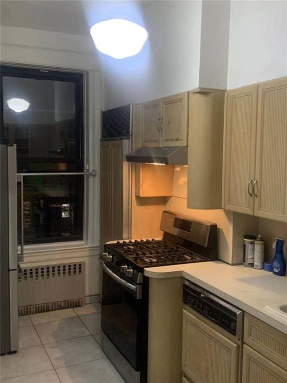 kitchen with under cabinet range hood, radiator heating unit, appliances with stainless steel finishes, light tile patterned flooring, and light countertops