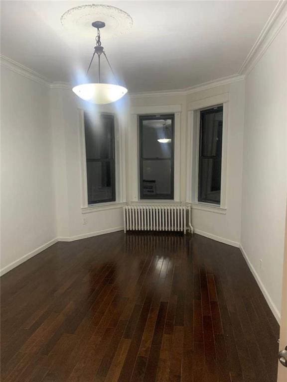 empty room with crown molding, radiator heating unit, wood finished floors, and baseboards