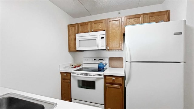 kitchen with white appliances, brown cabinetry, light countertops, and a textured ceiling