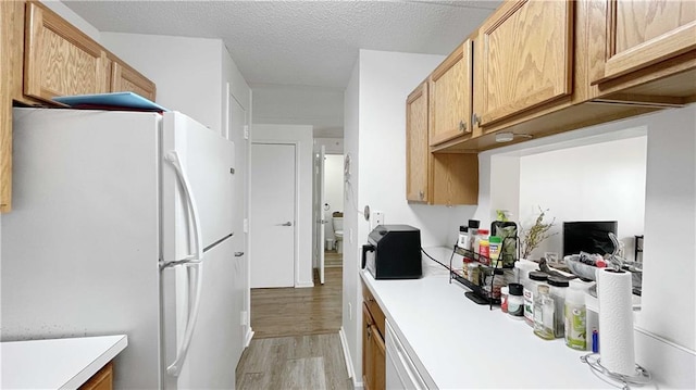 kitchen featuring a textured ceiling, light countertops, freestanding refrigerator, and light wood-style floors