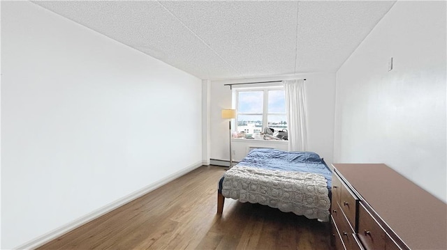 bedroom featuring a baseboard heating unit, baseboards, and light wood-style flooring