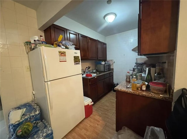 kitchen with stainless steel microwave, dark brown cabinetry, tile walls, and freestanding refrigerator