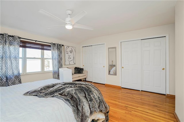 bedroom featuring a ceiling fan, baseboards, vaulted ceiling, light wood-type flooring, and two closets