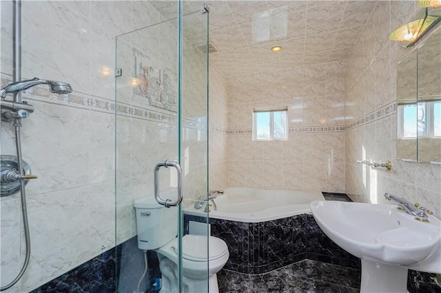 full bathroom featuring a shower with shower door, a tub with marble appearance, toilet, and tile walls