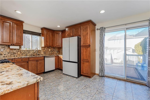 kitchen featuring dishwashing machine, brown cabinetry, freestanding refrigerator, and a sink