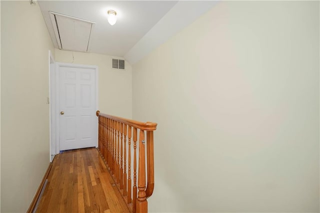 hallway with visible vents, wood finished floors, baseboards, attic access, and vaulted ceiling