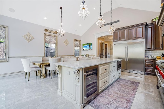 kitchen featuring built in refrigerator, wine cooler, arched walkways, light stone countertops, and hanging light fixtures