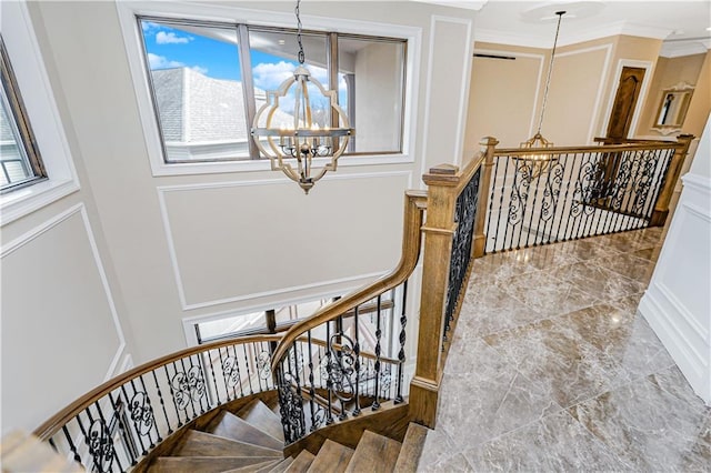 stairway with a chandelier, a decorative wall, marble finish floor, and crown molding