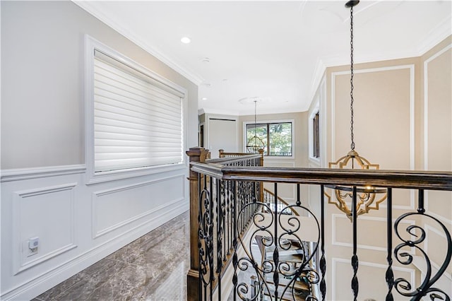 corridor with an upstairs landing, a decorative wall, wainscoting, and ornamental molding