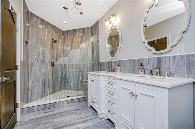 full bath featuring a marble finish shower, a sink, tile walls, and double vanity