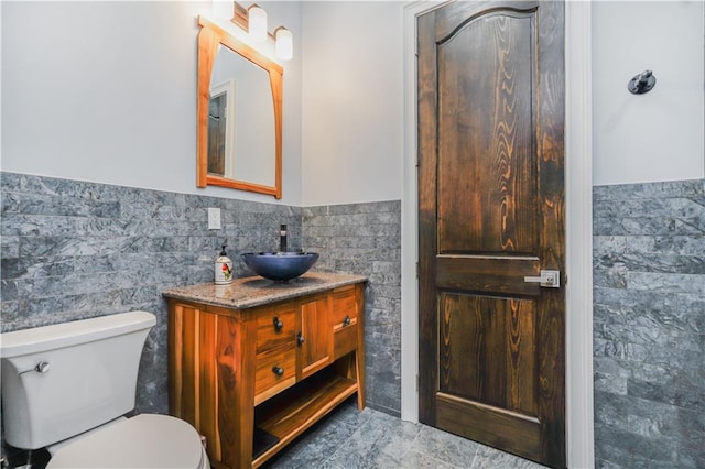 bathroom with a wainscoted wall, toilet, vanity, and tile walls