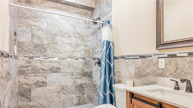 full bath featuring a wainscoted wall, toilet, a tile shower, tile walls, and vanity