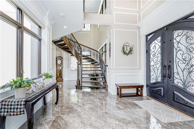 foyer featuring a decorative wall, marble finish floor, french doors, and plenty of natural light