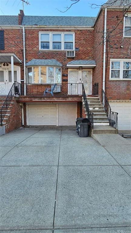 view of front facade featuring brick siding, a shingled roof, stairway, concrete driveway, and a garage