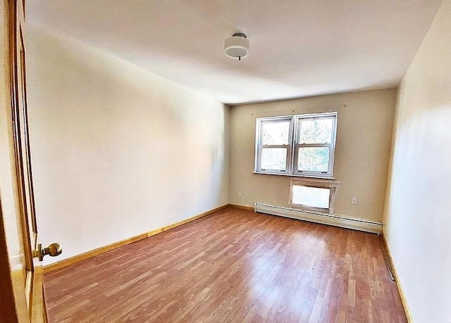 spare room featuring a baseboard heating unit, baseboards, and wood finished floors