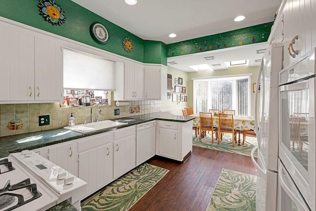 kitchen with dark wood finished floors, white appliances, dark countertops, and a sink