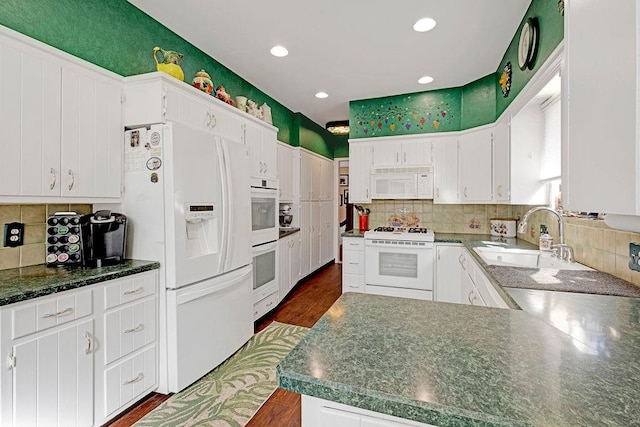 kitchen with backsplash, white appliances, white cabinetry, and a sink