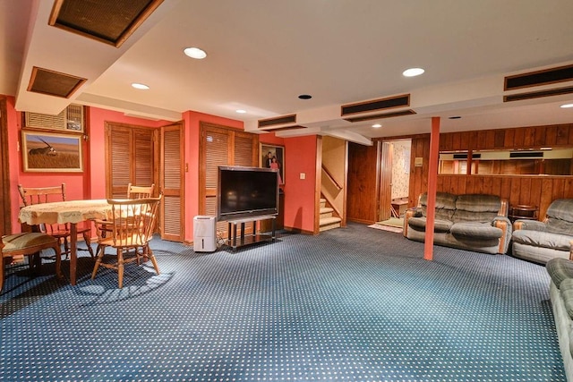 carpeted living room with recessed lighting, visible vents, wood walls, and stairs