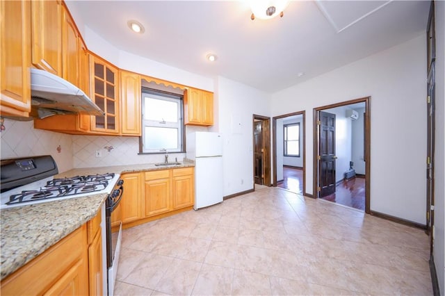 kitchen with under cabinet range hood, range with gas stovetop, decorative backsplash, freestanding refrigerator, and a sink